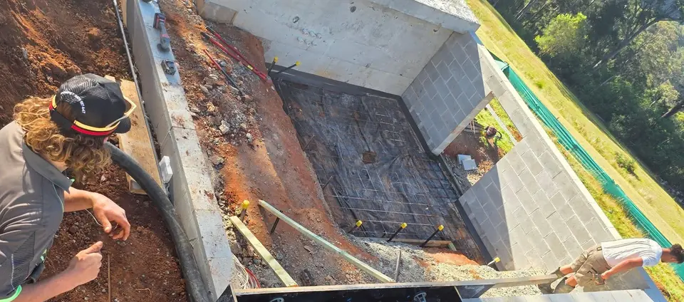 Crew member guiding the pump hose into stepped, reinforced formwork on a steep sloped site