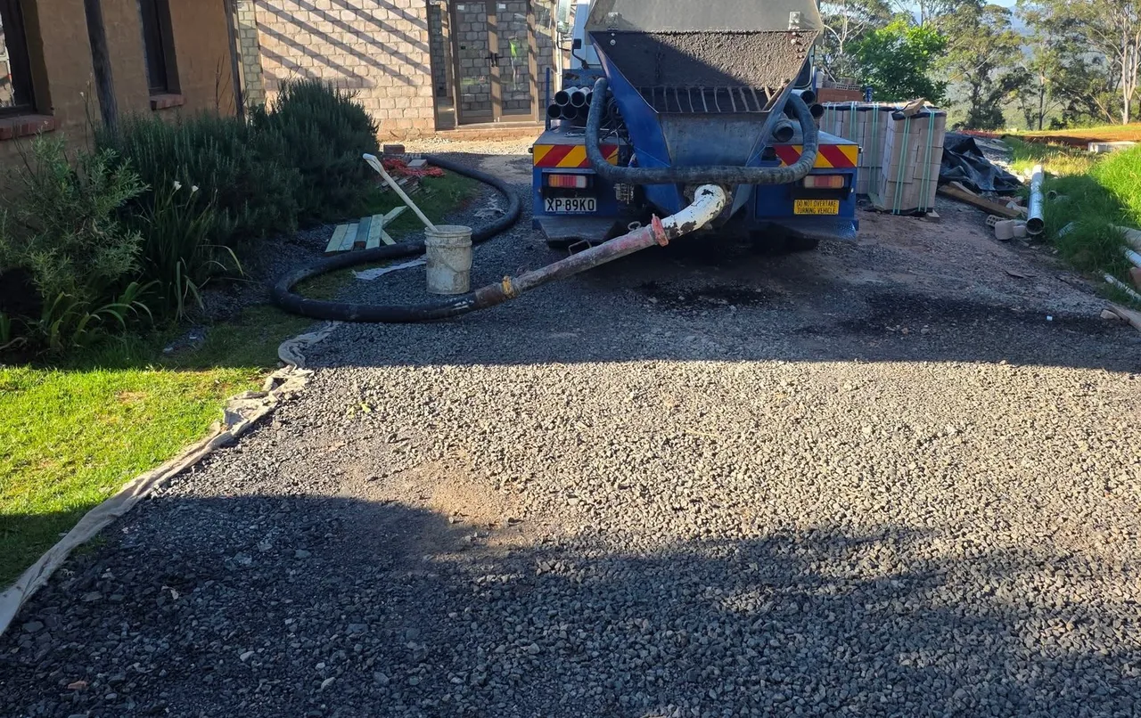 Concrete pump truck with hose running across a large gravel driveway on a South Coast property